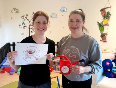 Johanna Fritz vom städtischen Familien- und Frauenbüro (l.) zu Besuch bei Tagesmutter Stephanie Fisch (r.) in ihren angemieteten Betreuungsräumen. Fritz übergibt eine bunte Gießkanne als kleines Dankeschön für die wertvolle Arbeit.